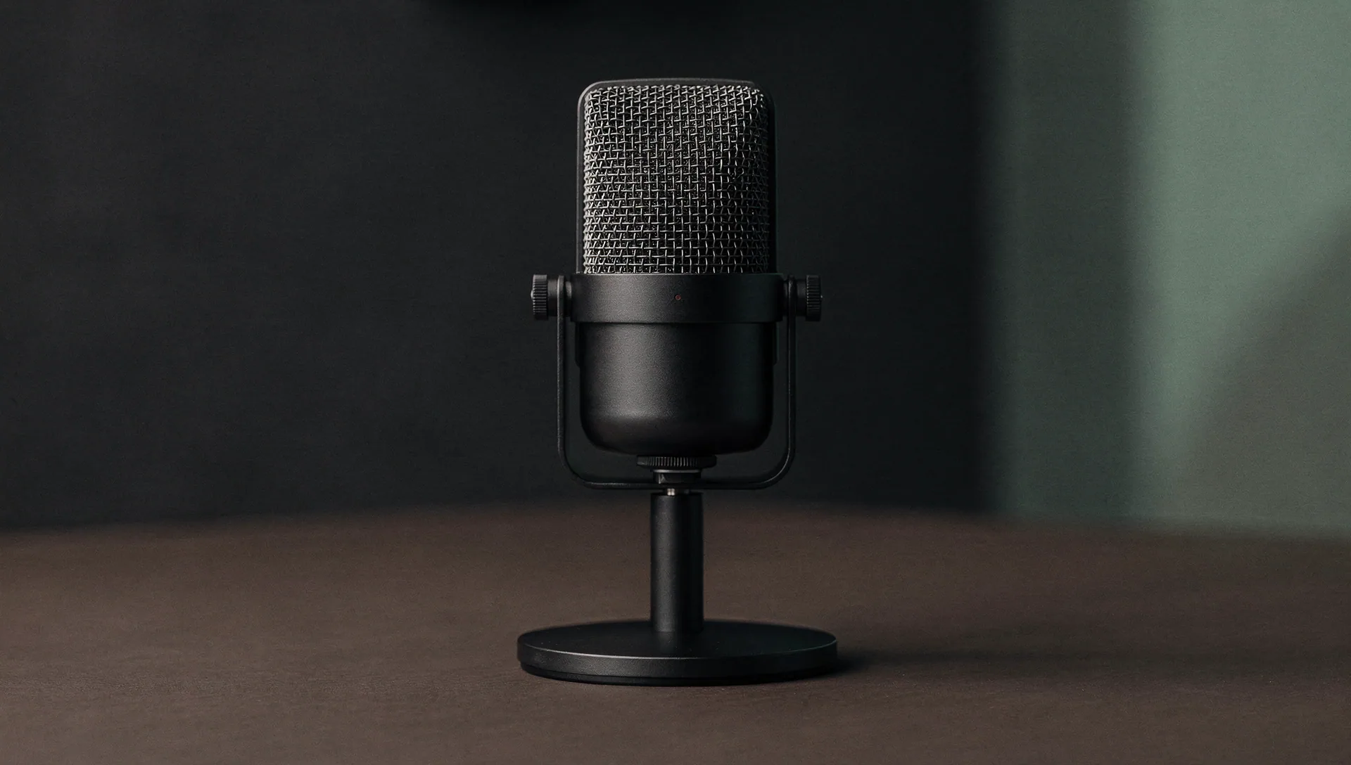Charcoal broadcast microphone on a minimalist desk in a softly lit media room